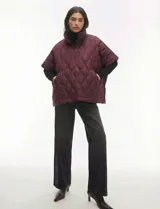 Poncho acolchado color vino tinto, con cuello alto y cierre frontal parcial. Presenta un patrón de costuras capitoné en forma de hoja o diamante y bolsillos delanteros.