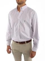 Camisa de corte clásico confeccionada en algodón, con diseño de rayas verticales finas en color rosa sobre fondo blanco. Presenta cuello abotonado, cierre frontal con botones, mangas largas con puños abotonados y un bolsillo en el pecho con el logo de la marca bordado.