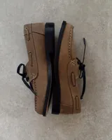 Zapato náutico de cuero vacuno color tostado, con cordones negros y suela plana de goma negra.