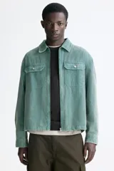 Sobrecamisa de pana de algodón color verde, con cuello clásico, cierre frontal de cremallera, mangas largas con puños abotonados y bolsillos superiores con solapa y botón.
