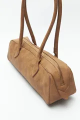 Cartera baguette cilíndrica con estampado de piel de serpiente en tonos beige y negro. Asas cortas y cierre superior con cremallera.