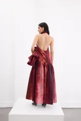 Vestido largo de corte holgado con estampado degradé en tonos rojizos y bordó. Presenta escote halter con cuello alto, espalda descubierta con cierre de botones y un maxi volado en la cadera que aporta volumen a la falda.