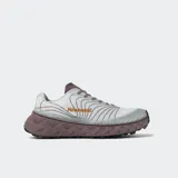 Championes de trail running Nnormal modelo Tomir, con diseño técnico en tonos gris claro y suela de plataforma robusta en color marrón oscuro. Presenta capellada con patrón de líneas curvas y logo de la marca en color naranja.