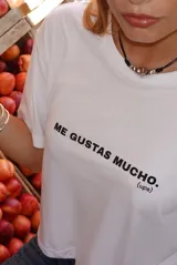 Remera blanca de manga corta con cuello redondo y texto estampado en negro en el pecho que dice "ME GUSTAS MUCHO. (ups)".