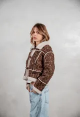 Campera de gamuza con estampado animal print de leopardo, forrada en corderito sintético color crema. Presenta cierre frontal con botones tipo toggle, cuello solapa y detalles de costuras visibles.