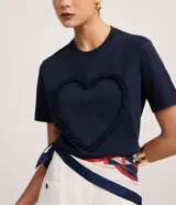 Remera marrón de algodón con cuello redondo y mangas cortas. Presenta un aplique de corazón con volados en el frente.