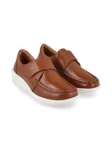 Zapato slip-on de cuero color camel con costuras visibles en la puntera, tira con cierre de velcro en el empeine y suela blanca con plataforma en cuña.