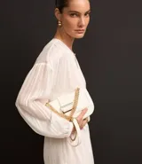 Blusa blanca de chiffon con cuello redondo y abertura en forma de gota en el frente. Tiene mangas 3/4 y rayas de hilo teñido metalizado.