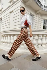 Pantalón de tiro alto y pernera recta con estampado de rayas verticales en tonos azul, marrón y beige. Incluye un cinturón delgado de color marrón oscuro con hebilla metálica dorada.