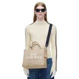 Bolso tote de lona color negro con estampado frontal en blanco que reza 'THE TOTE BAG MARC JACOBS'. Cuenta con doble asa superior, cierre de cremallera y correa larga ajustable y extraíble.