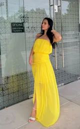 Vestido largo amarillo de estilo strapless, con cuerpo drapeado y falda fluida con tajo lateral.