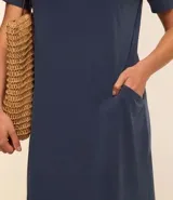 Vestido corto marrón oscuro, estilo camiseta, con escote redondo, mangas cortas y bolsillos laterales. El bajo es redondeado.
