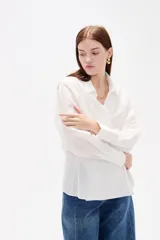 Camisa blanca de algodón con diseño cruzado y anudado lateral, cuello camisero y mangas largas con puños.