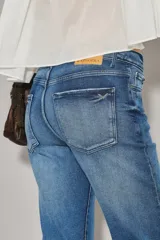 Jean de corte recto y tiro alto, confeccionado en denim azul con un lavado localizado que presenta efecto de bigotes y torceduras. Cuenta con cierre y botón frontal.