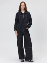 Buzo oversize negro de algodón con cuello alto y cierre frontal parcial metalizado. Cuenta con bolsillos laterales con cierre y diseño de mangas largas.
