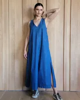 Vestido largo de denim azul, con escote en V, sin mangas, corte holgado, bolsillos laterales y aberturas en los costados de la falda.