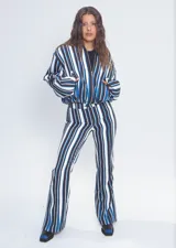 Campera tipo bomber corta, con cierre frontal, cuello a la base, bolsillos ojal y mangas largas abullonadas. Presenta un diseño estampado a rayas verticales en tonos azul, blanco y negro.