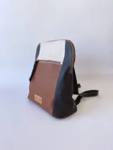 Mochila de cuero tricolor en tonos marrón tostado, negro y blanco, con bolsillo frontal con cierre, tiradores de cuero y detalle de etiqueta con logo grabado.