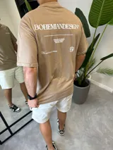 Remera oversize color marrón con estampado tipográfico blanco en la espalda que incluye la leyenda 'BOHEMIANDESIGN', texto secundario y un gráfico de cubo.