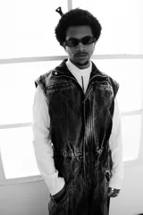 Mono de jean con lavado gris efecto desgastado, con múltiples cortes estructurales, cierre frontal oculto por cartera, cintura elástica y bordado de logo en azul. Incluye un pequeño accesorio de bolso desmontable para la cintura.