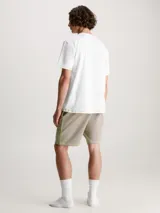 Conjunto de pijama Calvin Klein compuesto por una remera blanca con logo verde y un short beige con detalles en verde.
