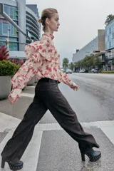 Blusa de cuello subido y manga larga con estampado floral en tonos rosados. Presenta un diseño con volantes en el pecho y a lo largo de las mangas, con cierre posterior mediante botones ocultos.