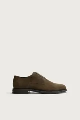 Zapato tipo derby de cordones, confeccionado en piel con acabado en serraje de color verde militar. Presenta horma redonda y suela plana en contraste de color negro.