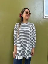 Remerón de manga larga con diseño de rayas horizontales finas en color negro sobre fondo blanco. Presenta un corte oversize, cuello redondo y un largo asimétrico con la parte trasera ligeramente más larga que la delantera.