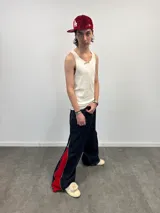 Pantalón de jean azul raw con diseño de corte versátil, ajustable mediante cierres laterales que revelan un panel interior rojo. Presenta una estampa gráfica de gran tamaño en la parte trasera con detalles bordados, costuras reforzadas y etiqueta de cuero en la cintura.