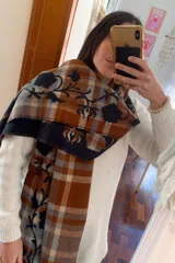 Bufanda de gran tamaño con diseño de cuadros en tonos naranja, beige y azul, decorada con un bordado floral en color azul oscuro y terminaciones con flecos.