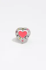 Anillo de metal plateado con diseño de corazón. Presenta un centro esmaltado en color rosado y un borde con letras de colores y detalles grabados.