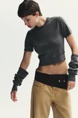 Jersey de punto gris oscuro, cuello redondo y manga larga. Presenta detalles desmontables con botones a lo largo de las costuras de las mangas y en el ruedo inferior.