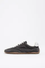 Zapatillas deportivas de perfil bajo confeccionadas en serraje color gris, con cordones claros y suela de goma con tachuelas características.