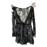 Vestido corto de encaje negro con diseño floral, escote en V profundo y mangas largas acampanadas. Presenta terminaciones con bordes festoneados.