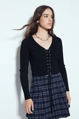 Top de tejido acanalado color negro, con escote en V y cierre frontal mediante cordones ajustables con ojales metálicos. Presenta mangas largas y un corte entallado al cuerpo.