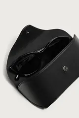 Funda para gafas de cuero negro con acabado abatanado, compartimento con cierre de botón a presión, pasador para cinturón y asa de mano.