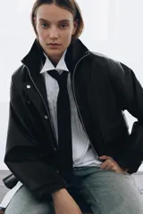 Chaqueta de corte oversize con acabado efecto piel. Presenta cuello alto, cierre frontal con cremallera y botones ocultos bajo solapa, bolsillos de plastrón con solapa en el delantero, mangas largas ajustables con trabillas y bajo ajustable con hebillas metálicas.