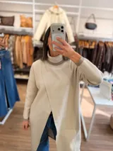 Polera larga de tejido de punto color beige, con cuello alto acanalado y diseño de tajo frontal cruzado. Presenta mangas largas con puños en tono contrastante y corte recto relajado.