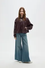 Chaqueta de eco-cuero color marrón oscuro, con cuello camisero, cierre frontal con botones, mangas largas abullonadas con puños y detalles de frunces en los hombros.