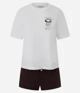 Conjunto de pijama compuesto por una remera blanca de cuello redondo y mangas cortas con estampa de café en el pecho, y un short marrón de cintura elástica con botones decorativos.
