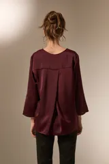 Blusa de satén color bordó con cuello en V y mangas tres cuartos. Presenta un diseño holgado con un pliegue central en el frente.