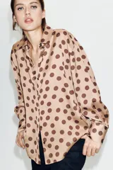 Camisa de corte clásico confeccionada en tela satinada, con estampado de lunares en contraste. Presenta cuello solapa, cierre frontal con botones y mangas largas con puños rectos.