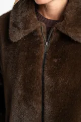 Abrigo de piel sintética en color marrón, con cuello clásico, cierre frontal con cremallera y mangas largas.