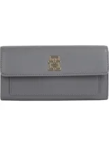 Billetera grande Tommy Hilfiger color gris con acabado granulado. Tiene cierre de solapa magnético, múltiples ranuras interiores para tarjetas, bolsillo exterior con cremallera e insignia del monograma TH en la solapa.