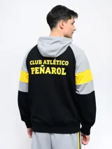 Campera deportiva negra con capucha y detalles en amarillo, cierre frontal y escudo del Club Atlético Peñarol en el pecho. Presenta cortes y cambios de color en mangas y cuerpo, y un estampado en la espalda.