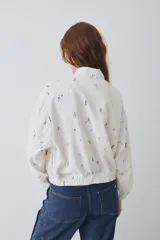 Campera tipo bomber de lino y algodón, con cierre frontal y puños elásticos. Presenta un estampado integral con motivos deportivos sobre fondo blanco.