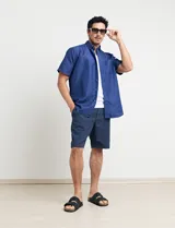 Camisa de manga corta azul con pequeños lunares blancos, cuello abotonado y bolsillo en el pecho.