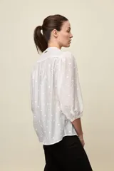 Camisa negra de textura liviana con detalle de lunares en relieve, cuello mao y cierre frontal con botones. Presenta mangas 3/4 con puños elastizados y frunces en los hombros.