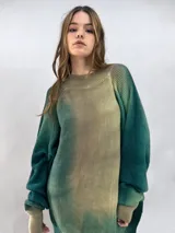 Buzo tejido de lana merino con diseño oversize, manga ranglan y cuello levemente elevado. Presenta un efecto de teñido degradado que combina tonos verdes y beige.