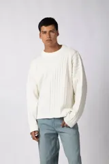 Sweater de punto color blanco con diseño asimétrico, presentando una mitad lisa y la otra mitad con textura de trenzas verticales. Posee cuello redondo y mangas largas con terminación en puño.